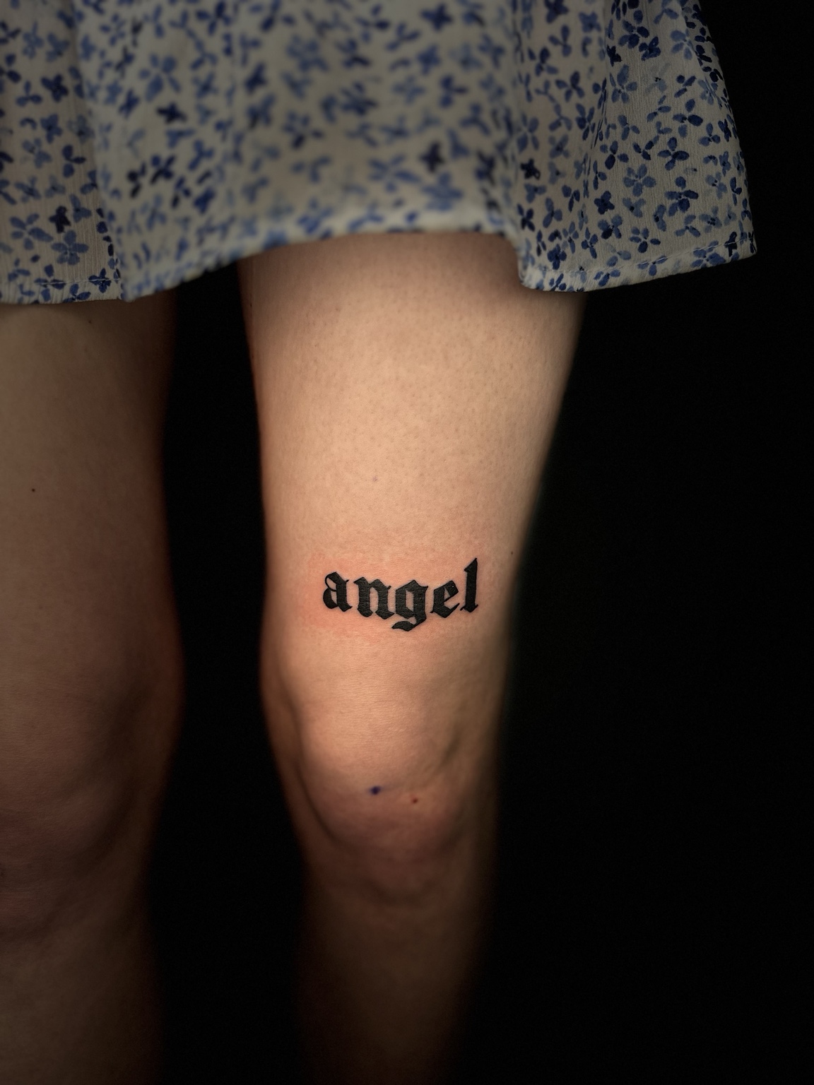 Tatuaż z napisem angel w stylu blackletter nad kolanem